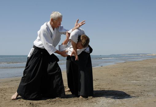 Two adults are training in Aikido on the beach