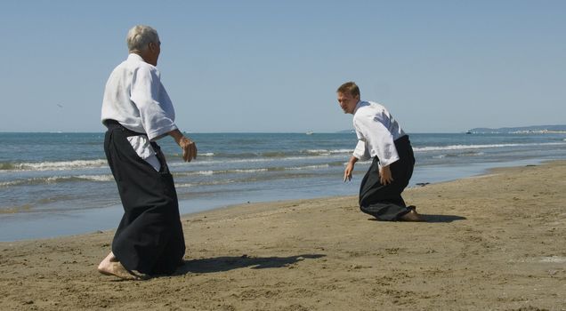 Two adults are training in Aikido on the beach