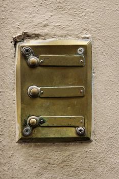 Three brass doorbells on a wall.
