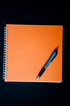 orange notebook and pen on black backround