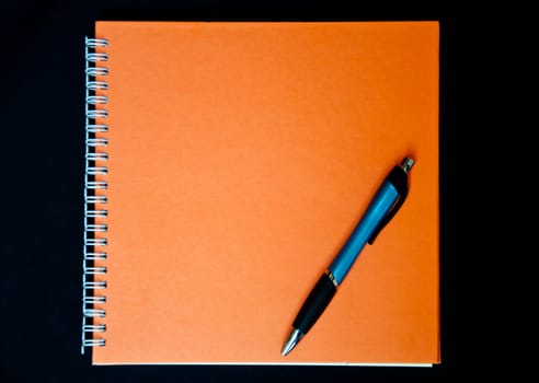 orange notebook and pen on black background