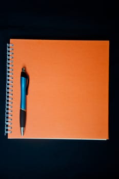 orange notebook and pen on black background