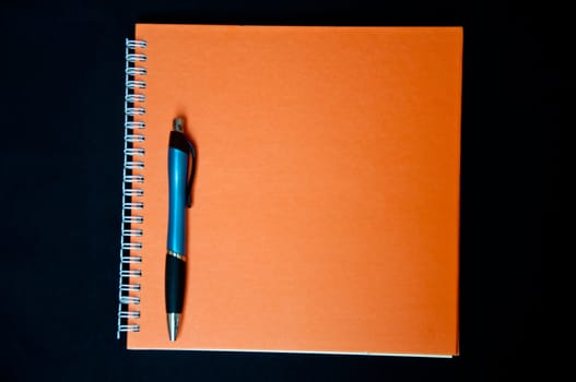 orange notebook and pen on black background