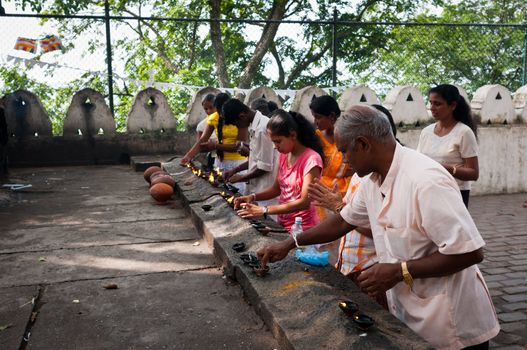 DAMBULLA, SRI LANKA - DECEMBER 07, 2011: People ignite oil lights in front of buddhist cave temple. Damsulla is a sacred place and Unesco world heritage site