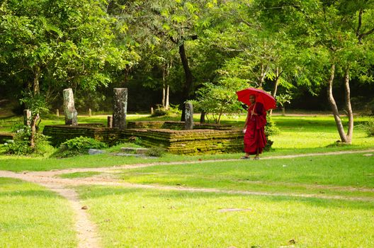 Anuradhapura, Sri Lanka - December 5, 2011:  Buddhism monk with red clothes and umbrella follow path in ruined old temple