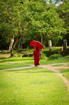 Anuradhapura, Sri Lanka - December 5, 2011:  Buddhism monk with red clothes and umbrella follow path in ruined old temple