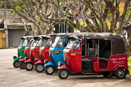 BENDOTTA, SRI LANKA - DECEMBER 04: Row of red blue and green tuk-tuks waits for passengers on December  4, 2011 in Bendotta, Sri Lanka. Tuk-tuk is a popular asian transport as taxi.