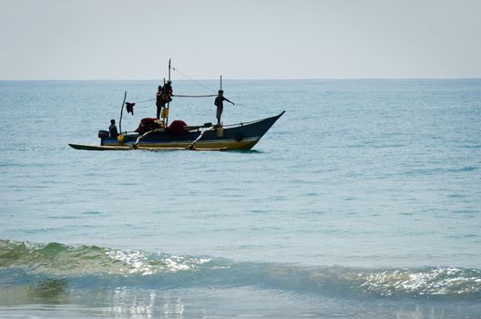 Mirissa, Sri Lanka - December 12, 2011: Traditional Asian small motorboat with four fishermen and fishing net