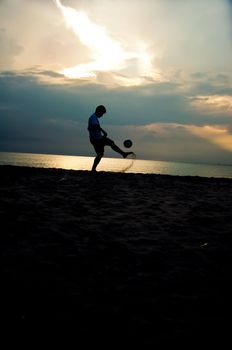 silhouette of man playing soccer on the beach