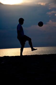 silhouette of man playing soccer on the beach