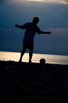 silhouette of man playing soccer on the beach