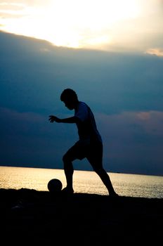 silhouette of man playing soccer on the beach