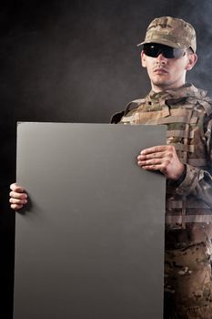 Modern soldier is holding a poster with smoke isolarted on black background