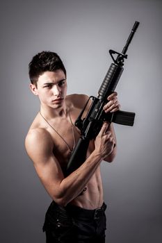 Handsome bare-chested soldier is holding a rifle on black background
