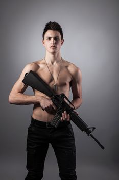 Handsome bare-chested soldier is holding a rifle on black background