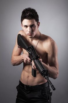 Handsome bare-chested soldier is holding a rifle on black background