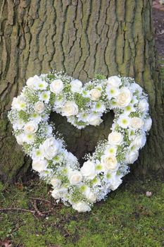 White heart shaped sympathy floral arrangement near a tree