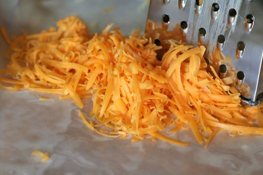 A pile freshly grated cheddar cheese, beside a cheese grater.
