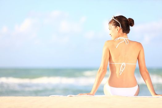 Beach holidays woman enjoying summer sun sitting in sand looking happy at copy space. Beautiful young bikini model. Mixed race Caucasian / Asian Chinese.