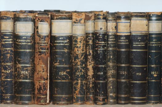 Row of old books on a bookshelf. Many of the books show lots of wear and damage from aging. The text in the book cover isn't a trademark