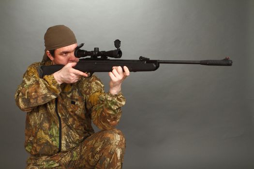 the man in a camouflage aims from a rifle with a riflescope