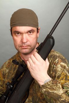 the man in a camouflage with a rifle in hands looks in a chamber lens.