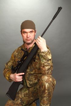 the man in a camouflage with a rifle in hands costs on one knee and looks in a chamber lens