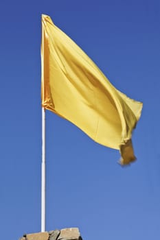 Vertical portrait of silky yellow flag against a deep blue sky