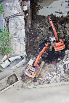 Construction site in Mumbai, India, two diggers working together to move soil onto a tipper truck, aerial view