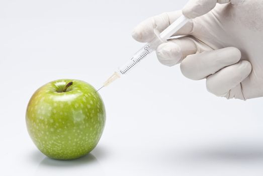 A gloved hand injecting an apple with a syringe on a white background.