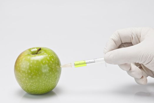 A gloved hand injecting an apple with a syringe on a white background.