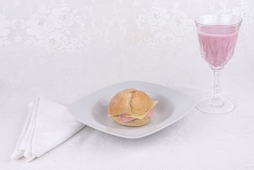 Strawberry shake in a glass and a bread with ham and cheese on a plate.
