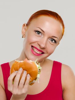 Beautiful young happy woman eating juicy burger and smiling