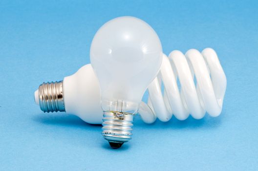 Novel fluorescent lights and old incandescent heat bulb on blue background. New technology for less electricity energy consumption.
