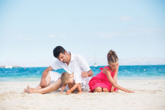 Happy family of three sitting and having fun on tropical beach