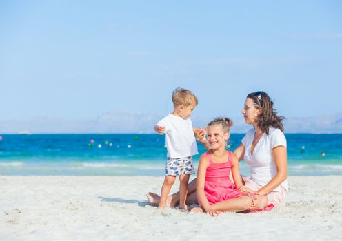 Happy family of three sitting and having fun on tropical beach