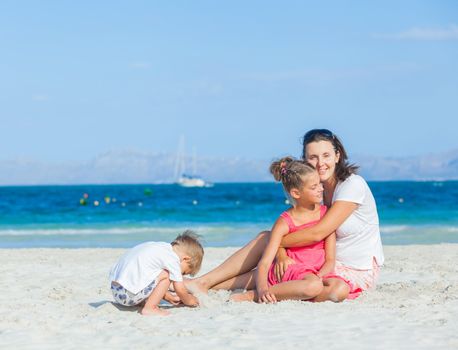 Happy family of three sitting and having fun on tropical beach