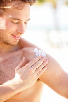 Sunscreen. Man putting sun screen / sun block on shoulder on sunny summer day during vacation on beach resort. Young handsome Caucasian male model smiling happy.