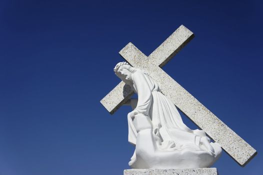 A statue of Jesus carrying the cross on blue sky background.