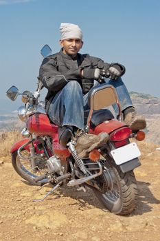 Indian motor biker sat back to front on red cruiser posing for the camera