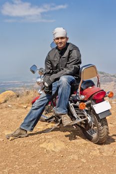 Young Indian motorcyclist on a hilltop and sat on his cruiser for a posed shot