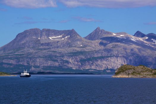 Picturesque scenery in norwegian fjord with high mountains and ferry passing through