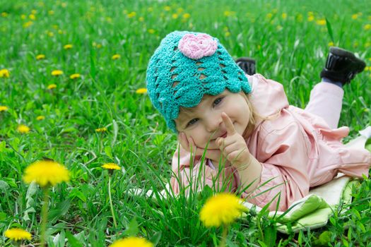 Smiling baby girl lying among field of dandelions