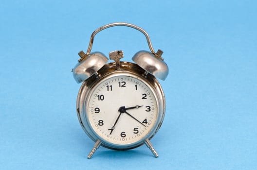 Retro grunge rusty alarm clock face made of steel on blue background.