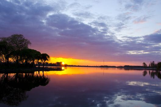 Amazing summer lake landscape and sunset colors in evening. Boats in distance. Sky and sun reflections.