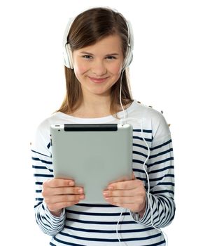 Smiling pretty girl holding i-pad. Headphones attached to it, listening to music