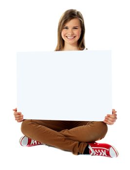 Smiling pretty teenager posing with blank placard, seated on floor