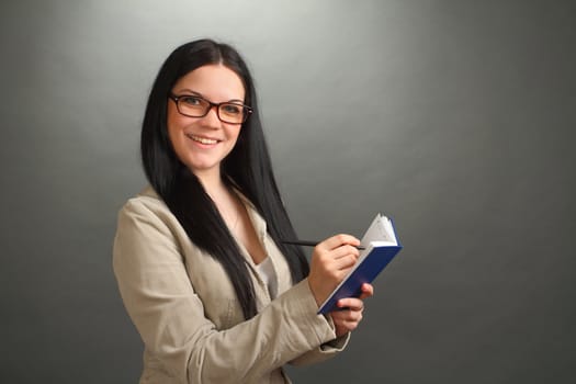 The girl, the brunette wearing spectacles with the handle and a notebook on a gray background