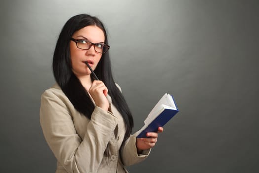 the thoughtful girl, the brunette wearing spectacles with the handle and a notebook on a gray background