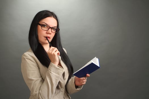 the thoughtful girl, the brunette wearing spectacles with the handle and a notebook on a gray background, looks in the chamber